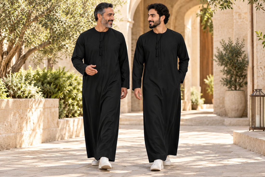 Father and adult son wearing Black Hamdan thobes with matching black trim in a courtyard