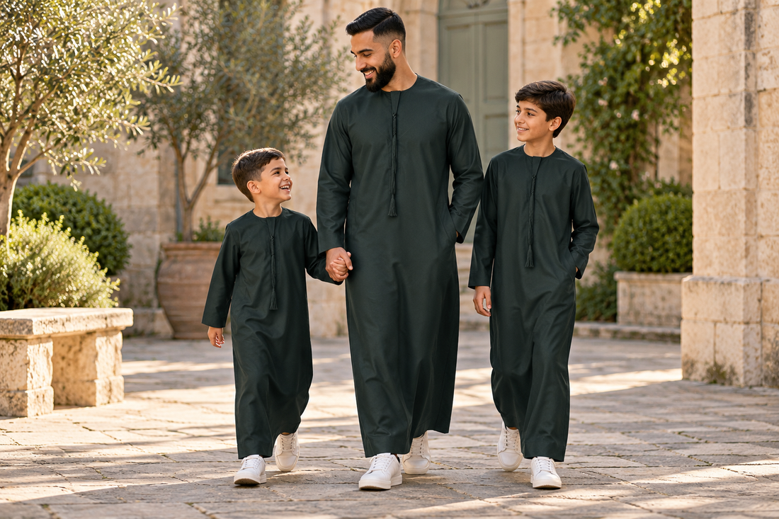 A father and two boys wearing green tassel thobes and white trainers, walking together through a sunlit courtyard.