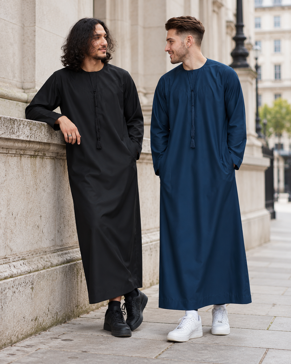 Two young adult friends wearing black and midnight blue tassel thobes with trainers on a city street.